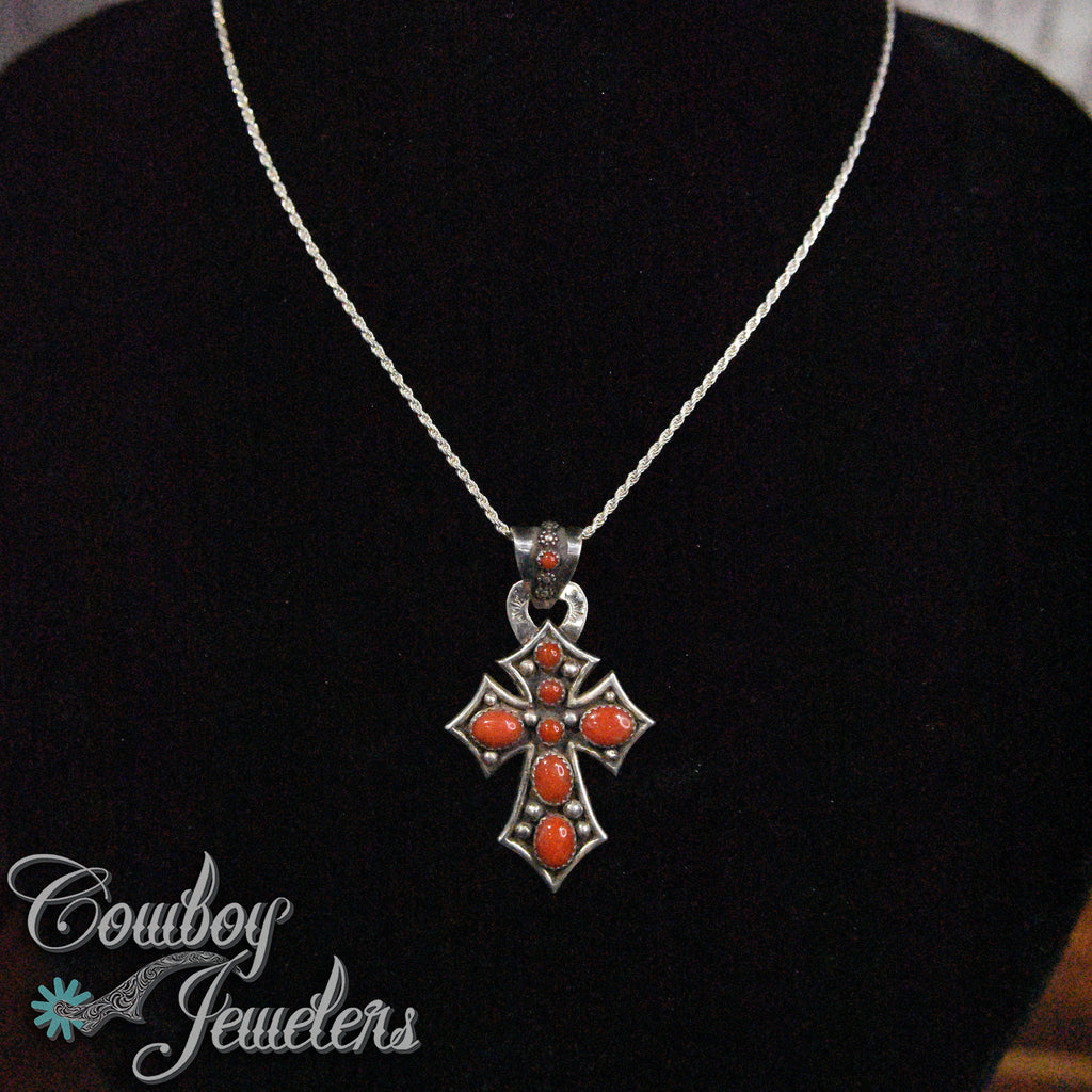 Silver cross pendant with red coral stones on a black background, branded 'Cowboy Jewelers'.