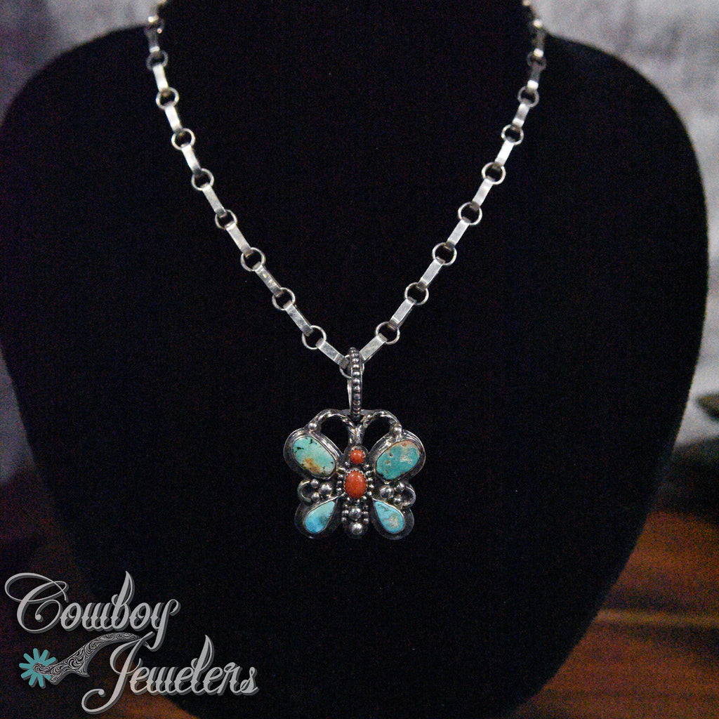Butterfly pendant necklace with turquoise and coral stones on a black stand with 'Cowboy Jewelers' branding.