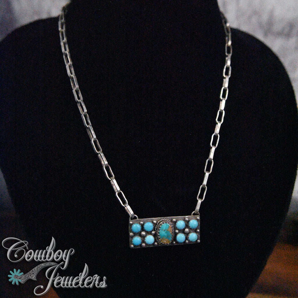 Necklace with turquoise stones on a black stand, branded 'Cowboy Jewelers'.
