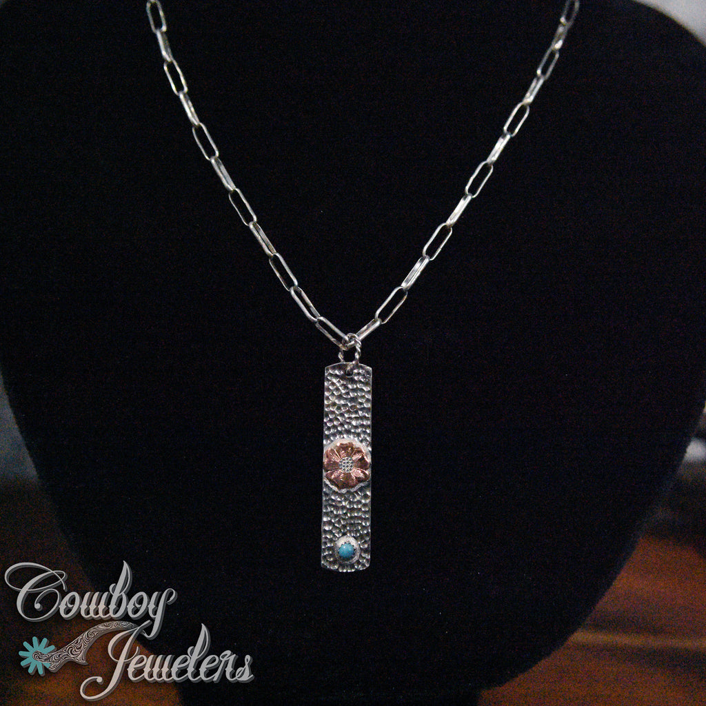 Silver necklace with a flower and turquoise pendant on a black background, featuring 'Cowboy Jewelers' branding.