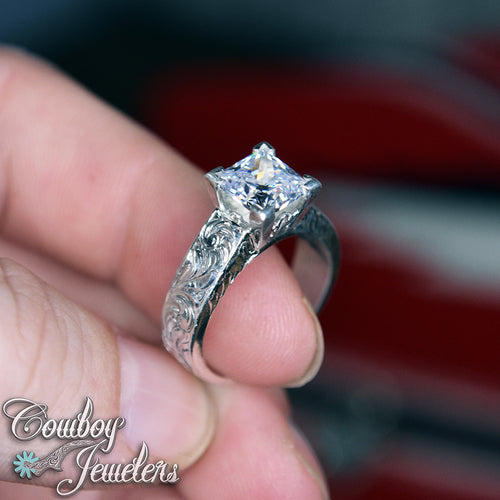 Silver ring with a diamond held in a hand, brand 'Cowboy Jewelers' visible