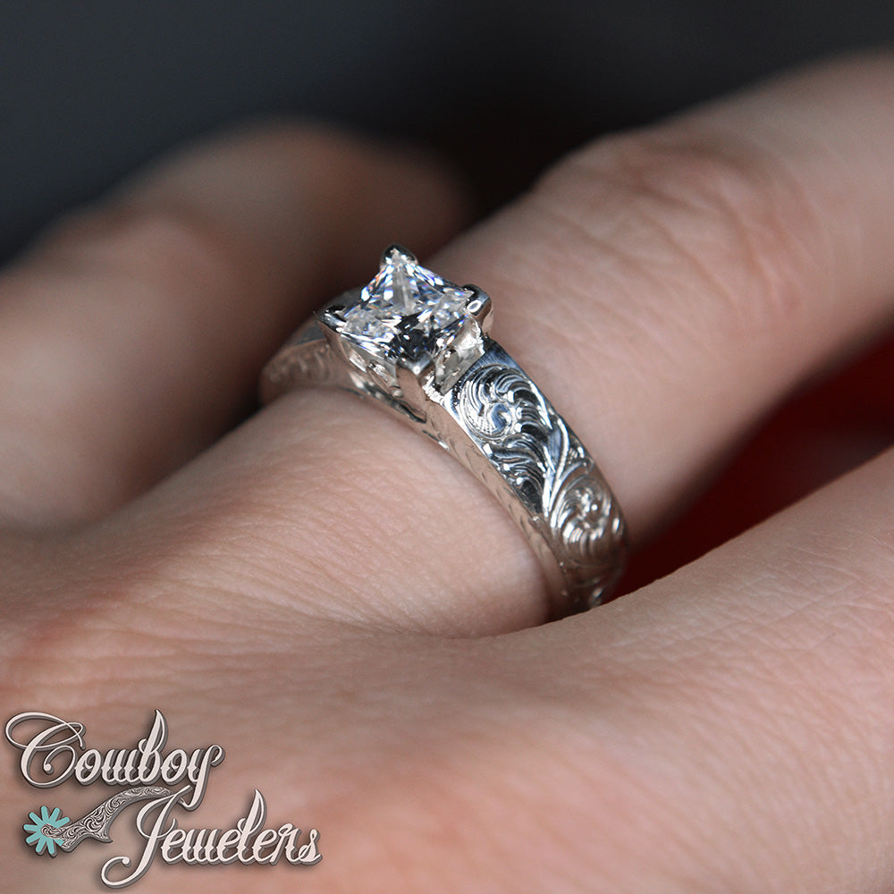 Silver ring with a diamond on a finger, branded 'Cowboy Jewelers'.
