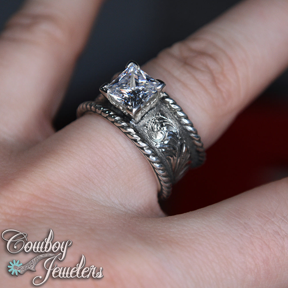 Rope edge Silver ring with a diamond on a finger, branded 'Cowboy Jewelers'.
