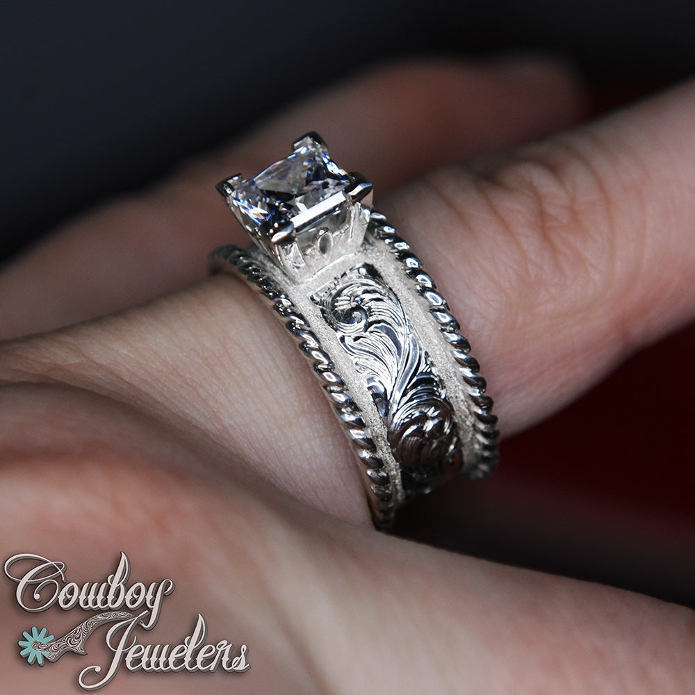 Silver ring with diamond on a finger, branded 'Cowboy Jewelers'.