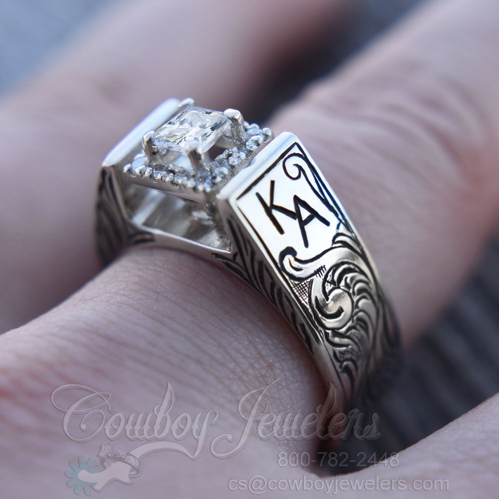 Silver ring with diamond on a finger, branded 'Cowboy Jewelers'.