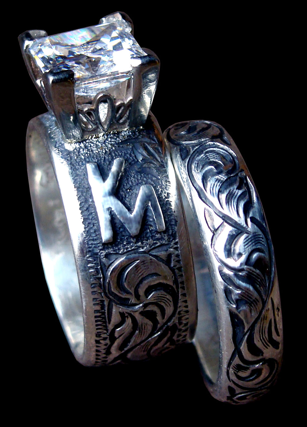 Silver ring with intricate designs and a prominent 'K' on a black background