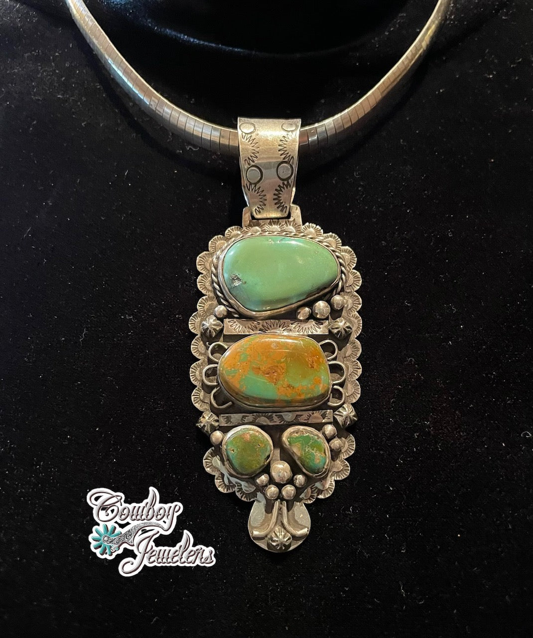 A sterling silver pendant necklace with royston turquoise stones, displayed on a black velvet jewelry bust. A 'Cowboy Jewellers' logo is visible in the bottom-left corner.